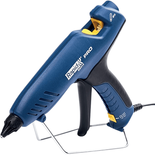 L’image montre un pistolet à colle électrique posé sur une surface. Le pistolet à colle est bleu et jaune et comporte une petit embout noir à l’avant. Il est branché à une prise électrique à travers un long câble.